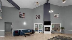 A spacious living area with a blue sofa, a fireplace, and artwork on the walls. - AmericInn by Wyndham Lake Mills (Lake Mills)