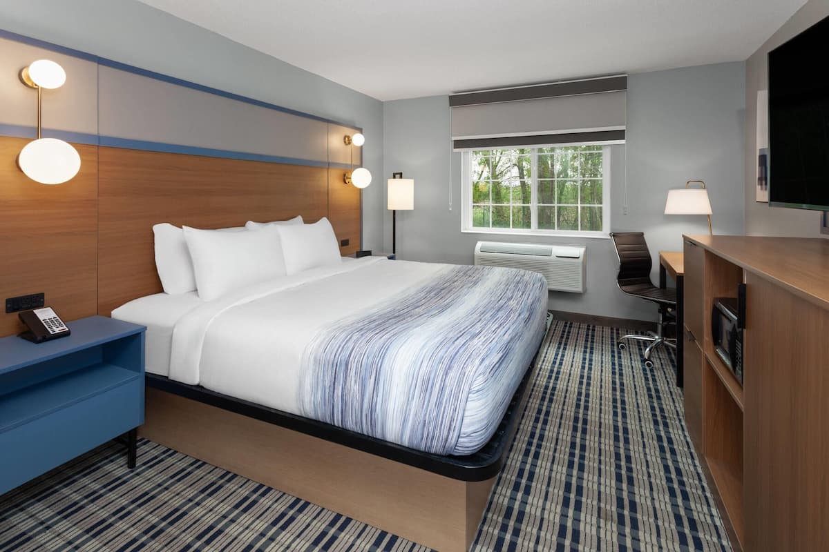 A hotel room with a bed, bedside table, lamp, desk, chair, TV, and window.