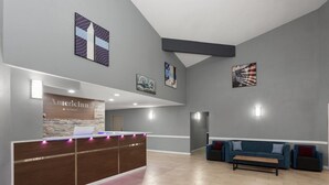 A reception area with a wooden reception desk, a blue sofa, and artwork on the walls. - AmericInn by Wyndham Lake Mills (Lake Mills)