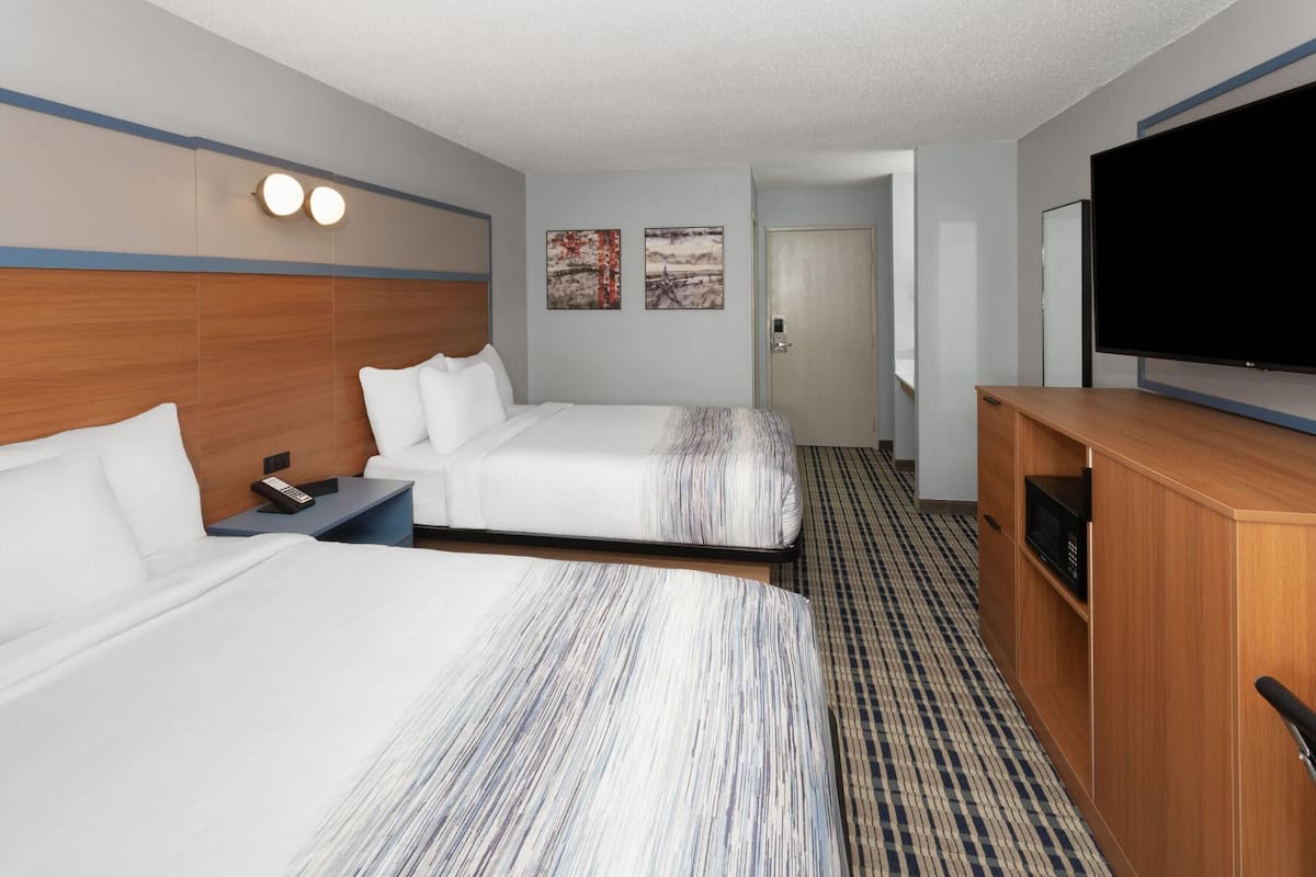A hotel room with two beds, a TV, a desk, and a door leading to another room.