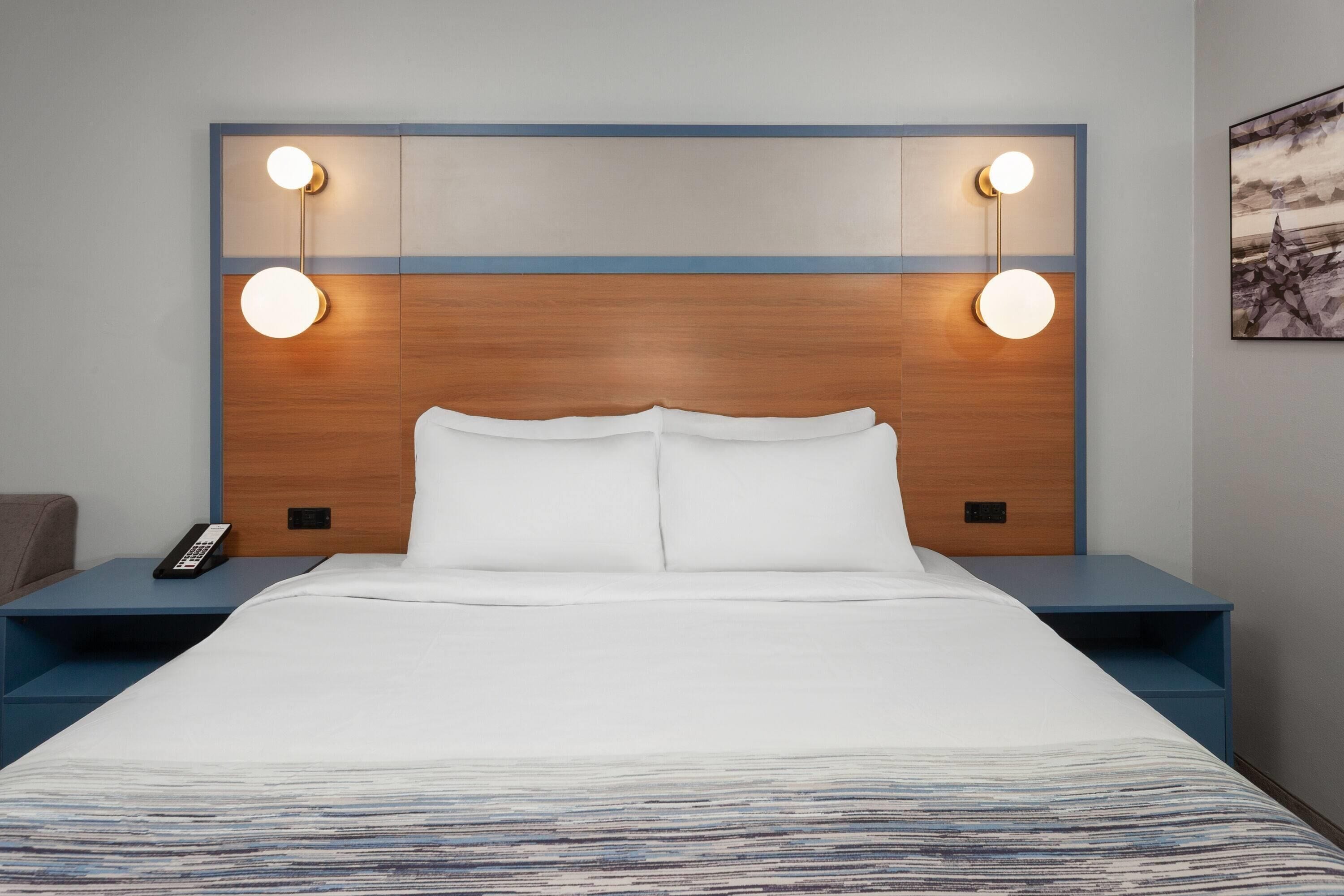 Een hotelkamer met een groot bed, twee nachtkastjes, een afstandsbediening en wandlampen.