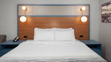 Ein Hotelzimmer mit einem großen Bett, zwei Nachttischen, einer Fernbedienung und Wandleuchten.