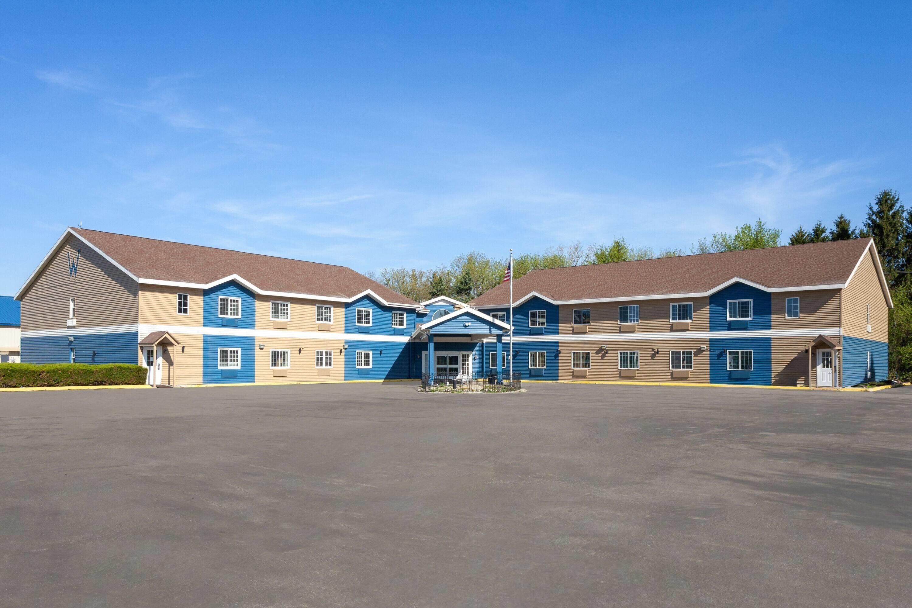 Un hôtel à plusieurs étages, doté d’une entrée principale, d’un grand parking et surplombant un ciel d’un bleu éclatant.