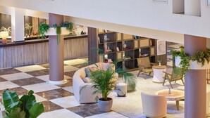 Een ruime lobby met een zwart-wit betegelde vloer, zithoeken en potplanten.