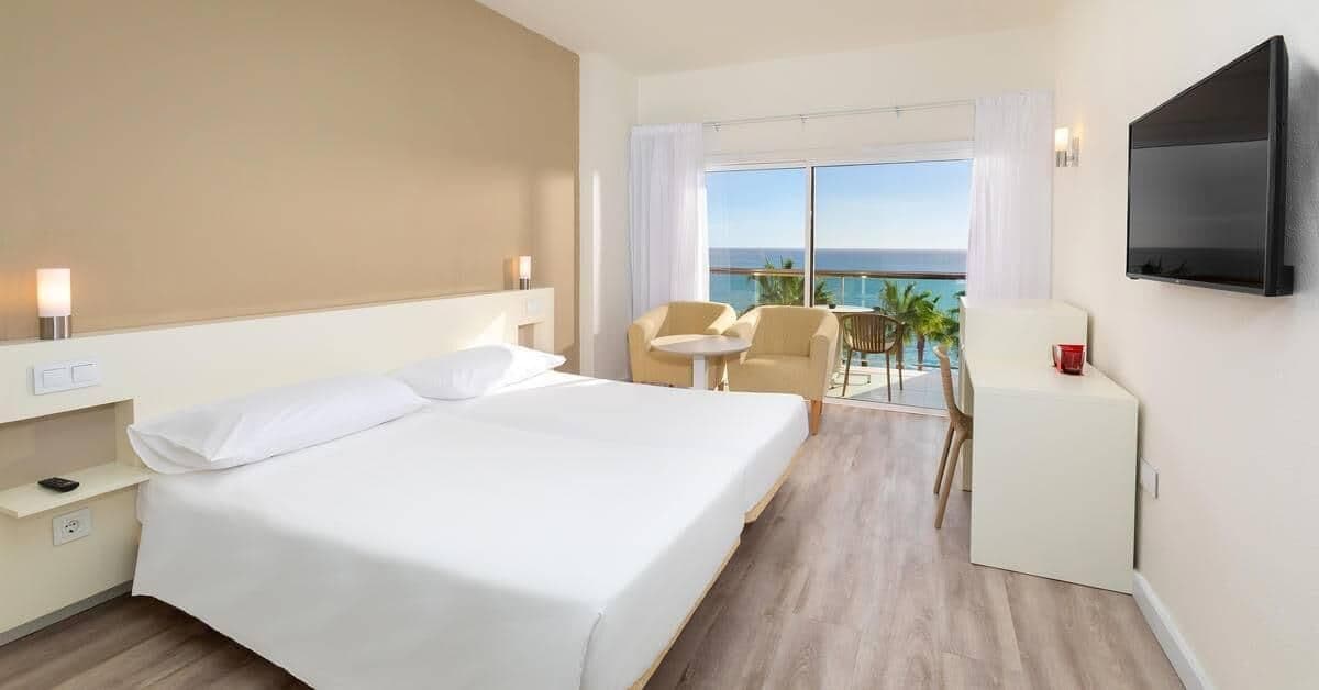 A hotel room with a large bed, a desk, a chair, and a TV.