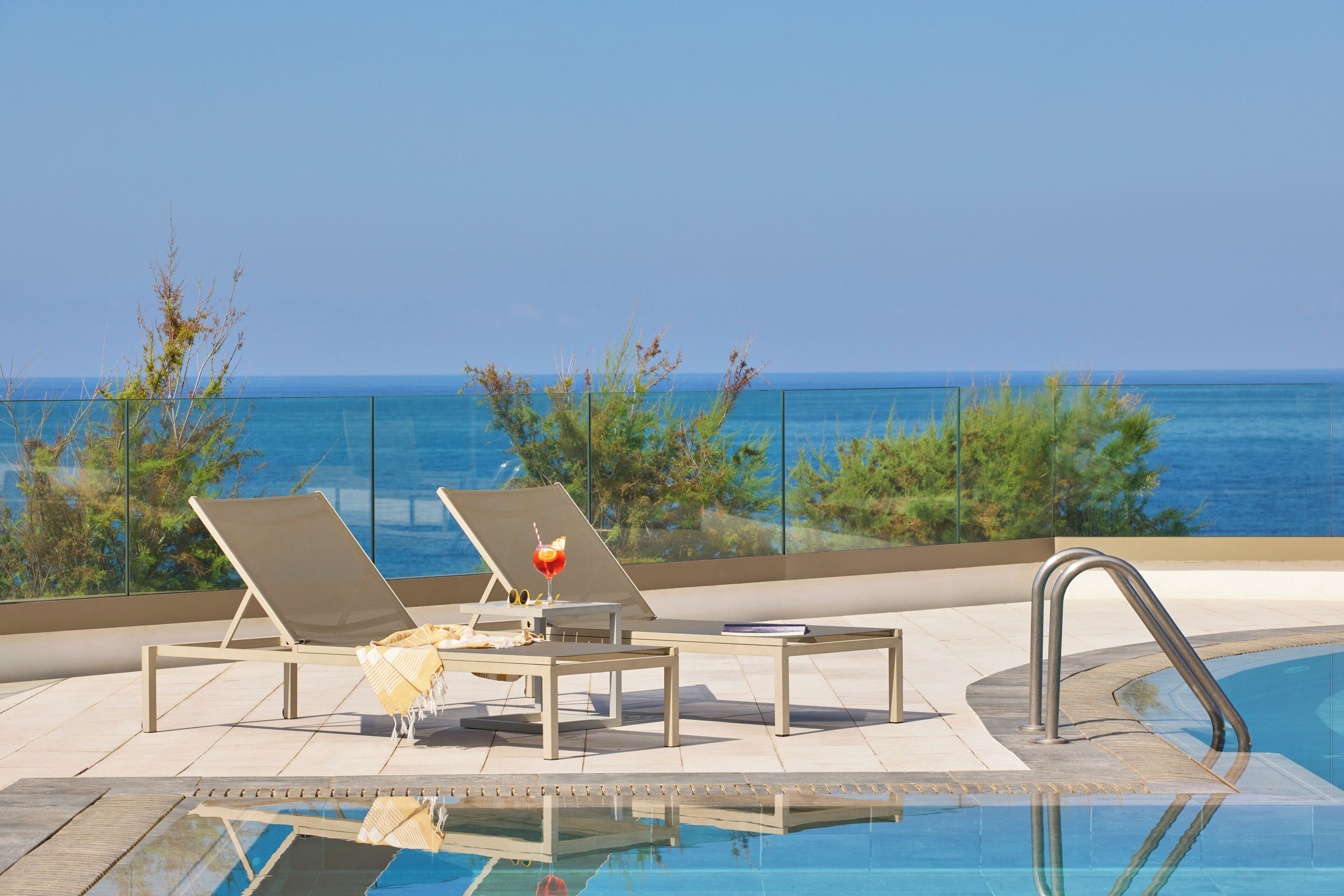 Zona de piscina con sillones de descanso y una mesa, con vista al mar.