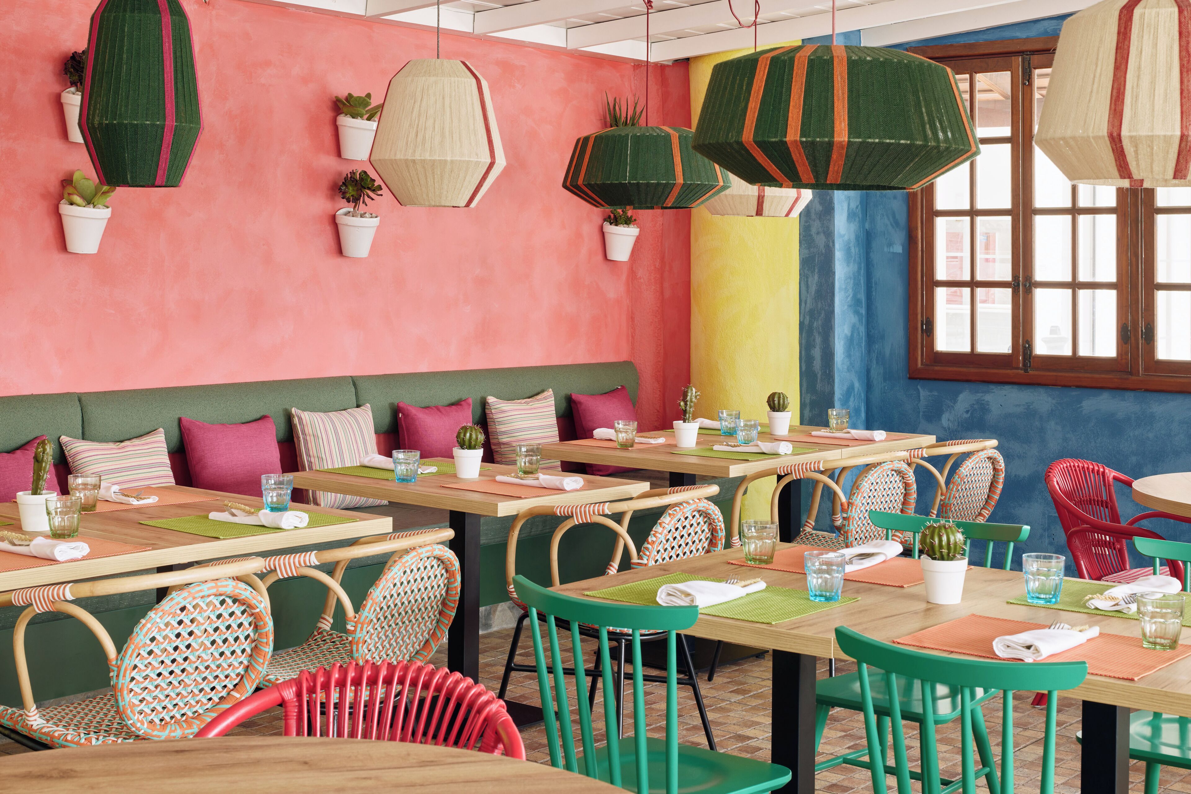 Un restaurant doté de nombreuses tables et chaises, de plantes en pot et de lanternes en papier suspendues.