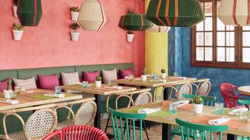 Un restaurant doté de nombreuses tables et chaises, de plantes en pot et de lanternes en papier suspendues.