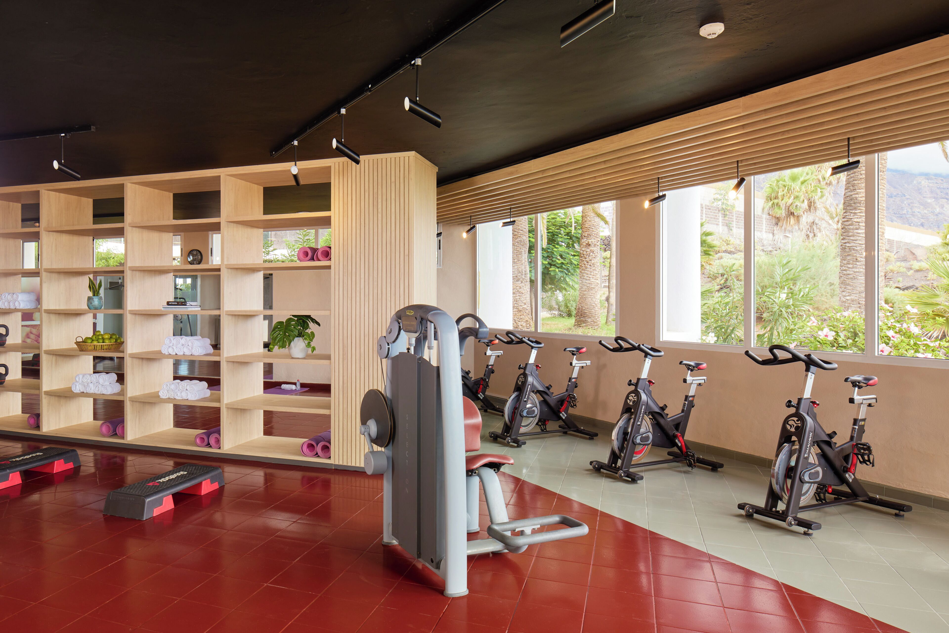 Un gimnasio con equipo de ejercicio, una pared con estanterías y ventanas grandes.