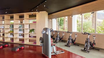Un gimnasio con equipo de ejercicio, una pared con estanterías y ventanas grandes.