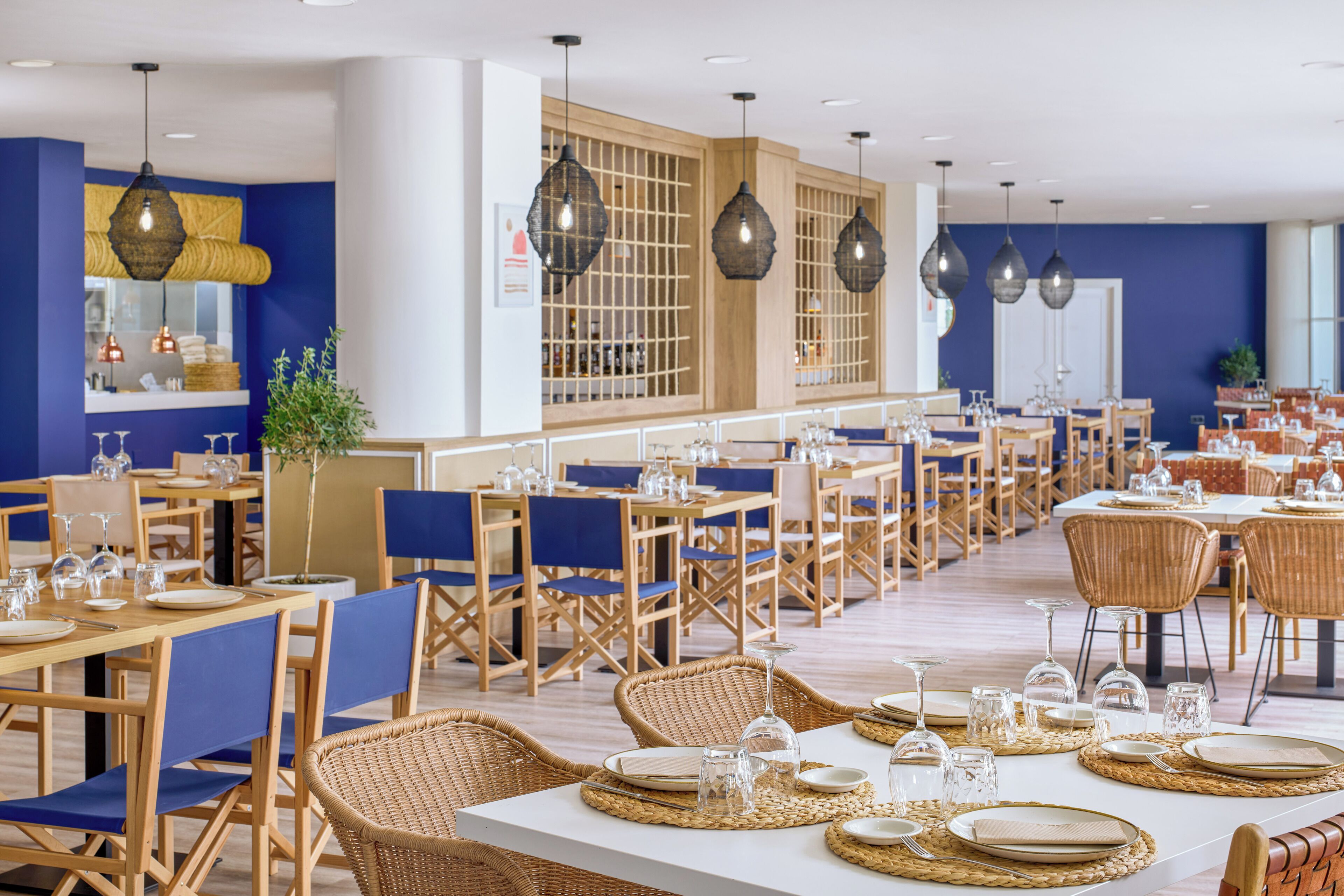 Un restaurante con varias mesas y sillas, algunas con individuales tejidos y otras con manteles blancos.
