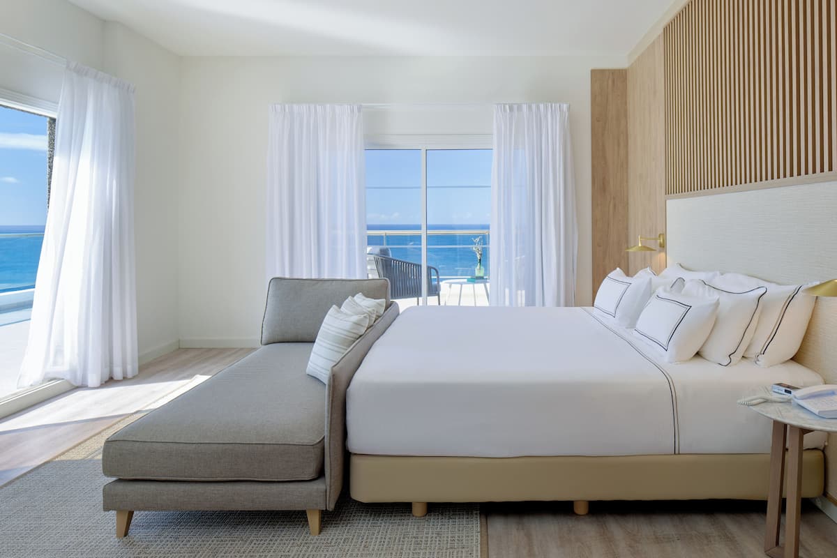 Une chambre d’hôtel moderne avec un grand lit, un canapé, une petite table et une vue sur l’océan.