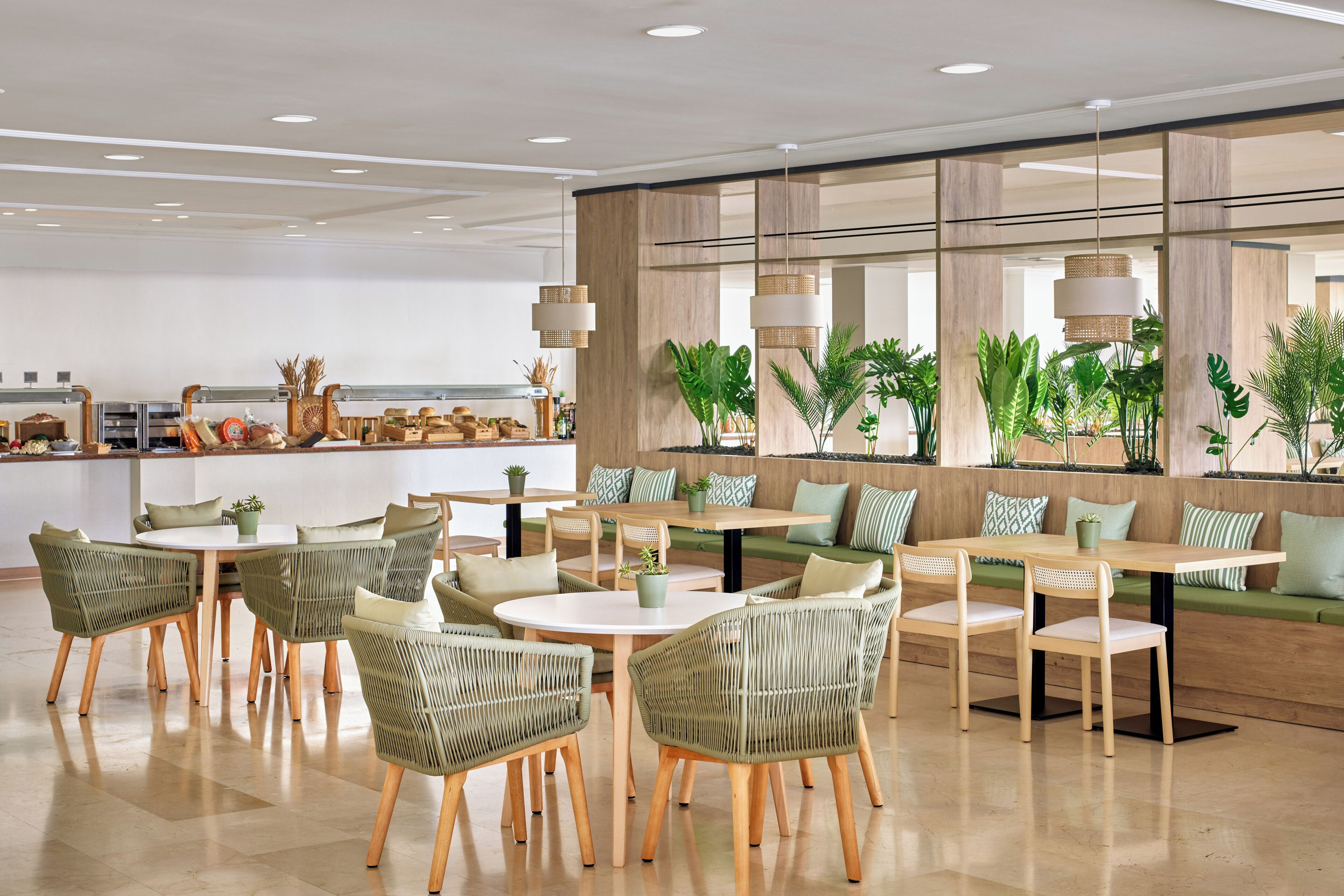 A modern dining area with wicker chairs and tables, a kitchen in the background, and a large window with plants.
