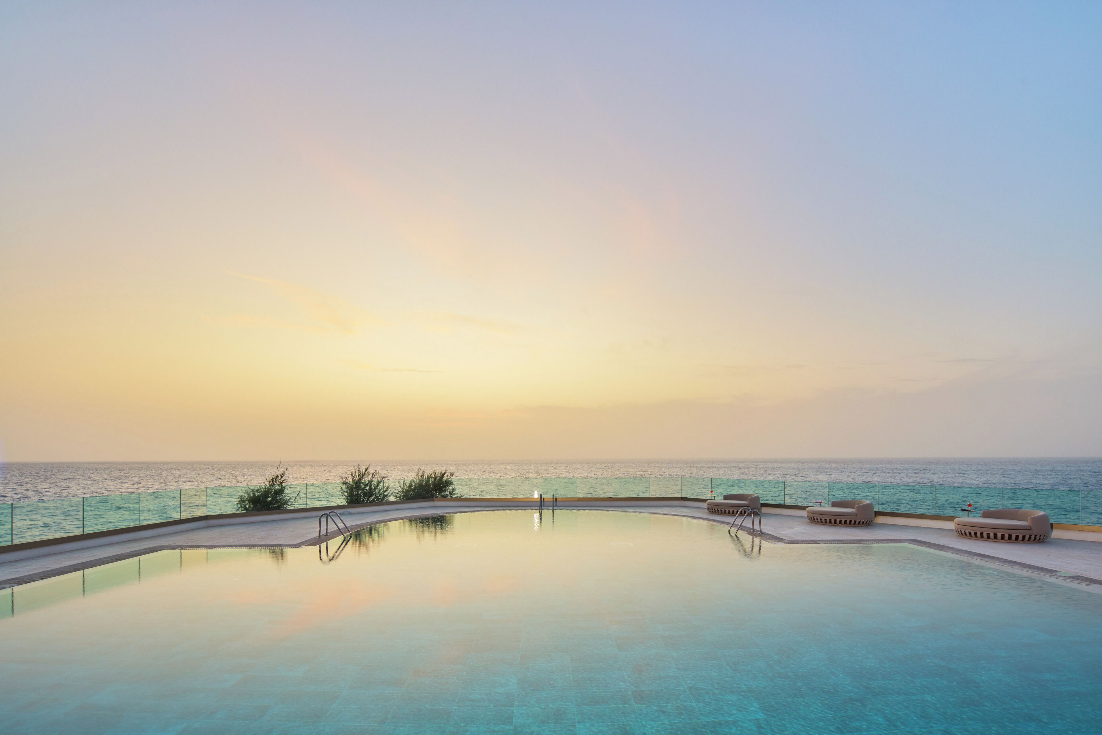 A serene infinity pool with a clear view of the ocean at sunset.