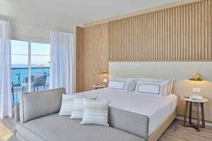 Habitación de hotel moderna con una cama grande, un sofá, vista al mar y un panel de pared de madera.