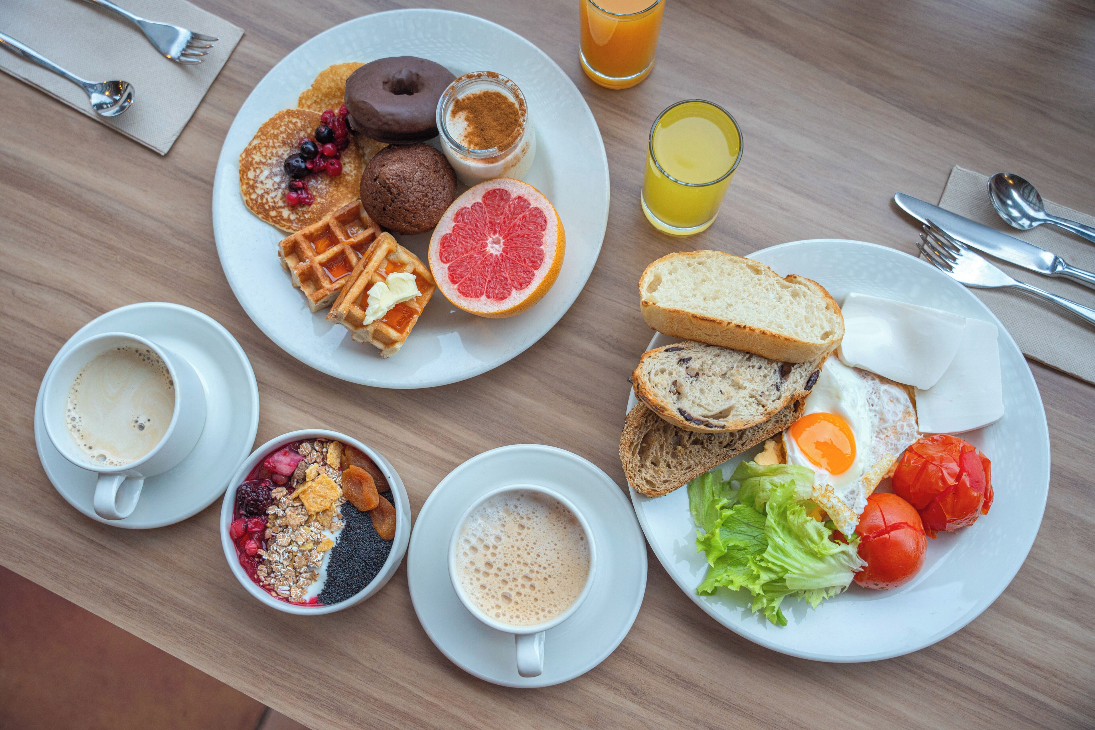Ein Frühstücksbuffet mit Waffeln, Pfannkuchen, Toast, Eiern und Früchten auf Tellern, dazu Kaffeetassen und Saftgläser.