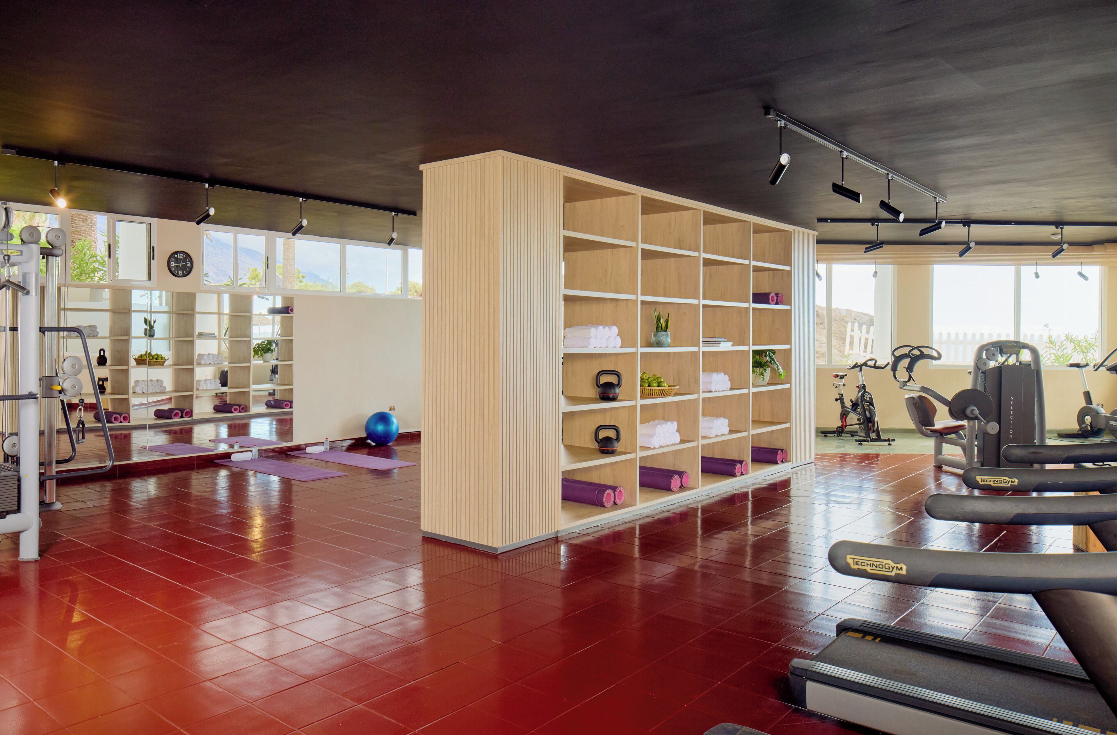 Une salle de sport équipée de matériel d’exercice, un meuble de rangement en bois et un sol recouvert de carreaux rouges.