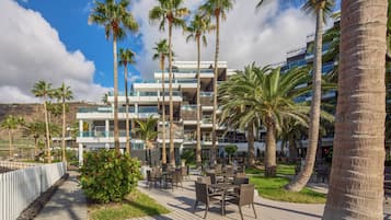A resort with outdoor seating, palm trees, and a modern building with balconies.
