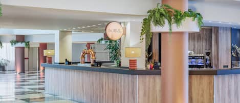 A hotel lobby with a reception desk, a large column with greenery, and a check-in counter.