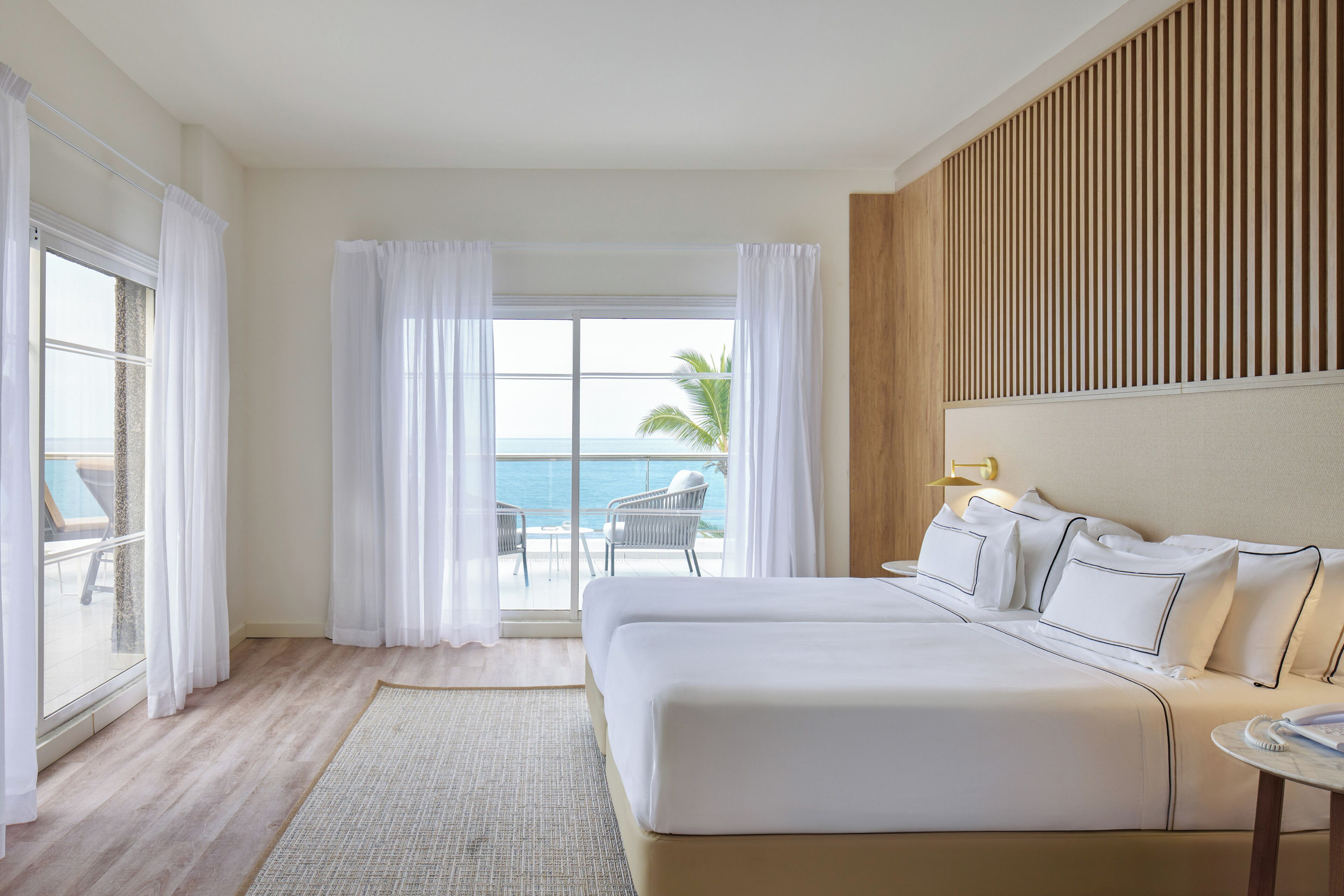 A hotel room with a large bed, a view of the ocean, and a balcony with a chair.