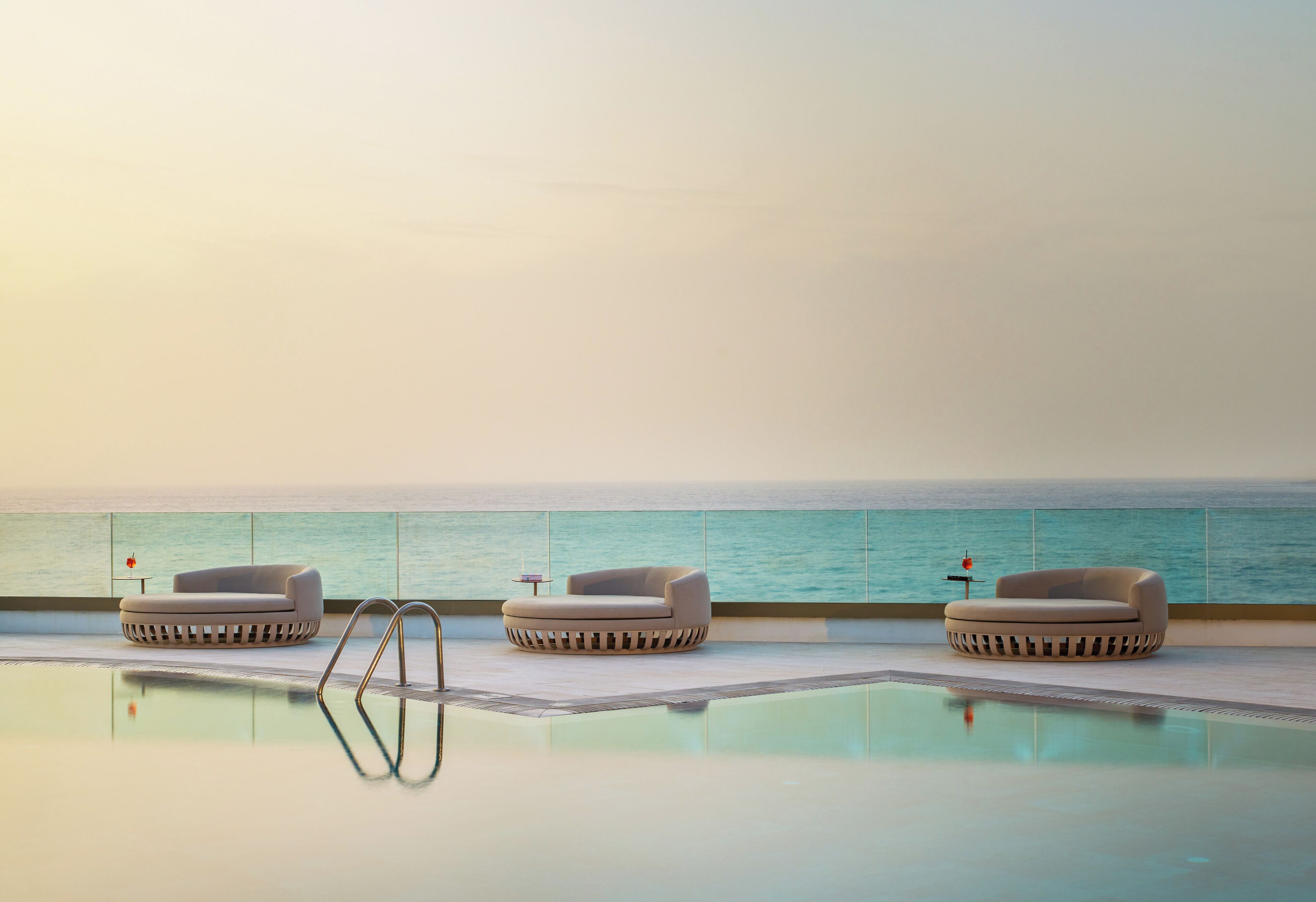 A poolside area with three lounge chairs and a small table, overlooking a body of water.