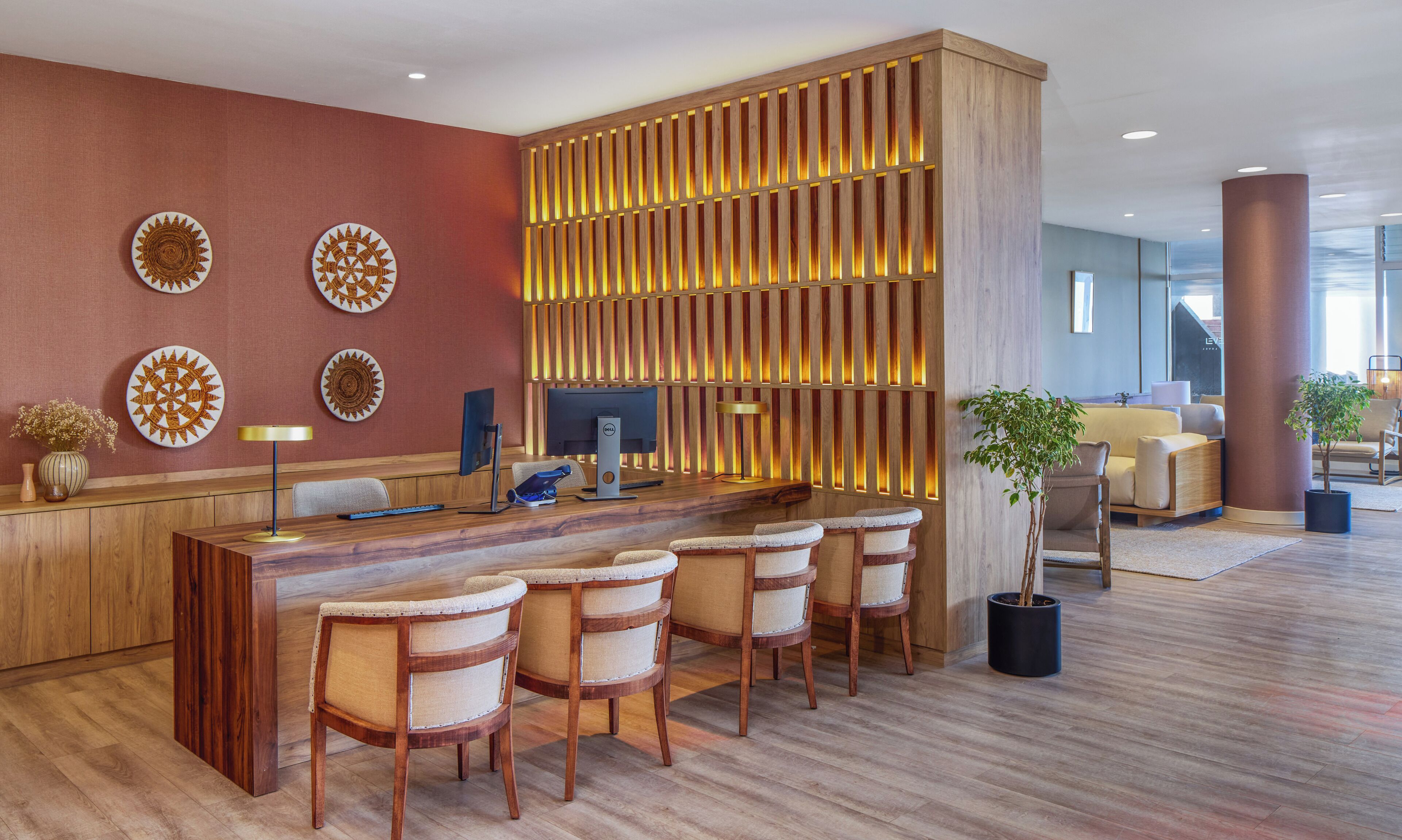 A reception area with a wooden desk, four cushioned chairs, a computer, and decorative plates on the wall.