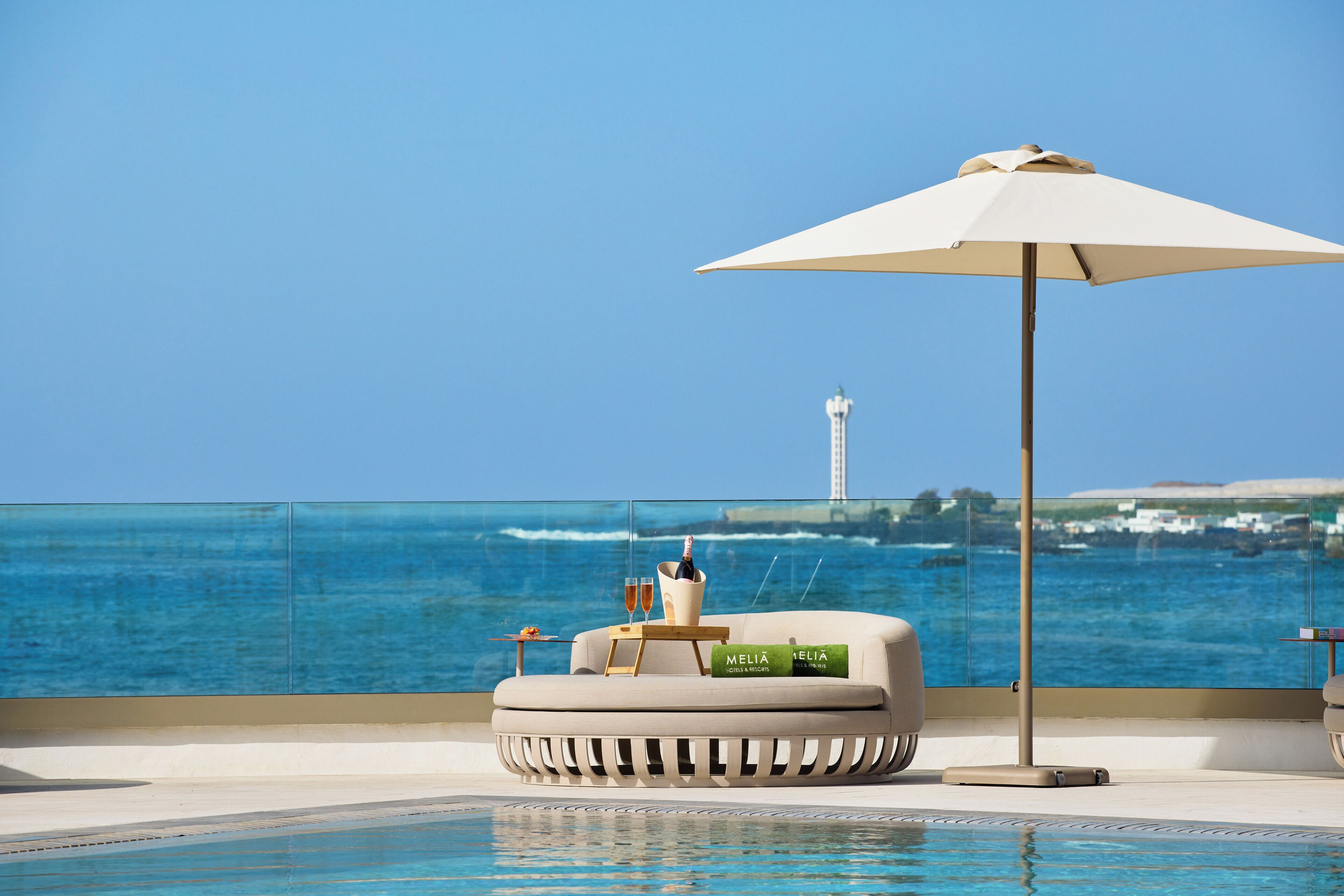 Zona de sofàs al costat de la piscina amb vista al mar i un far al fons.