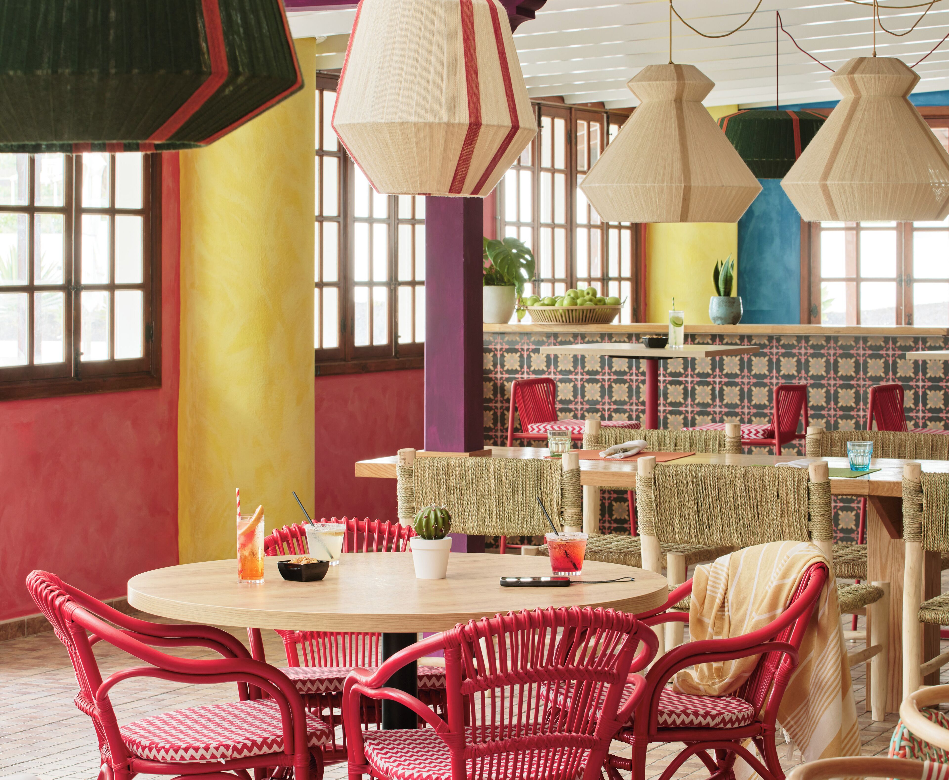Un espace repas avec des tables rondes, des chaises en osier rouge et des luminaires suspendus.