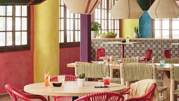 Un espace repas avec des tables rondes, des chaises en osier rouge et des luminaires suspendus.
