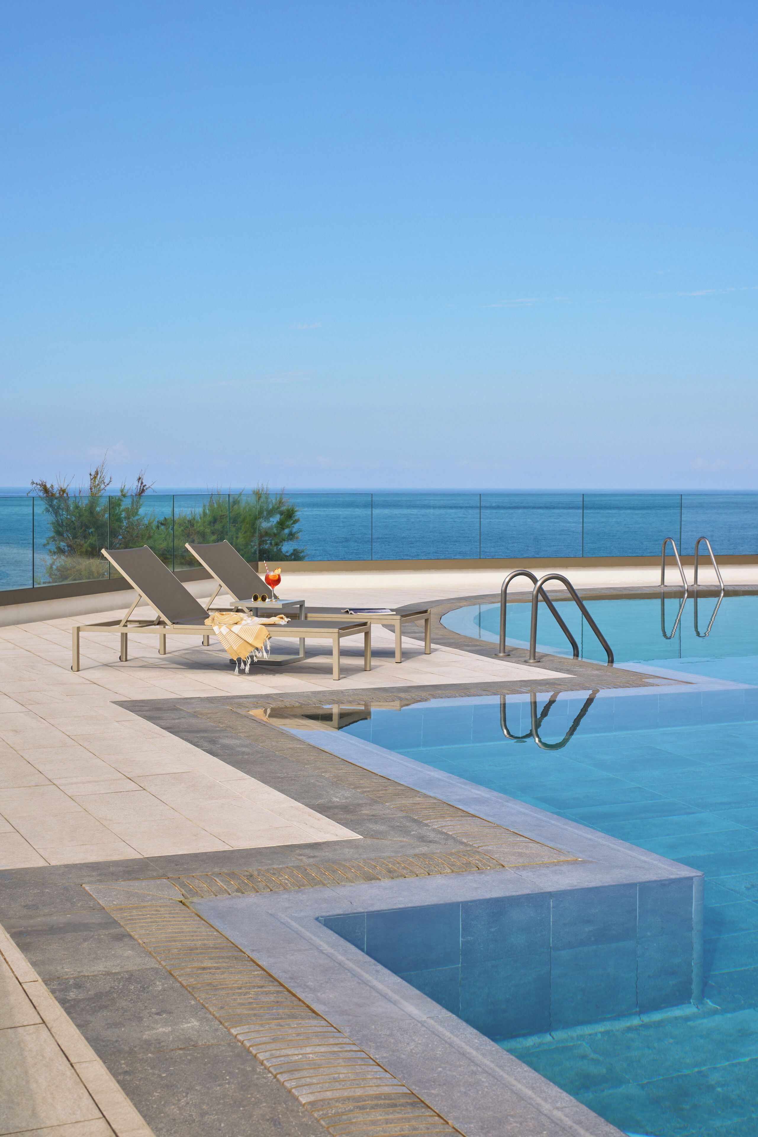 Zona de piscina con sillas de descanso y vista al océano.
