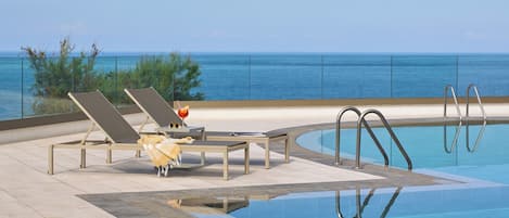 A pool area with lounge chairs and a view of the ocean.