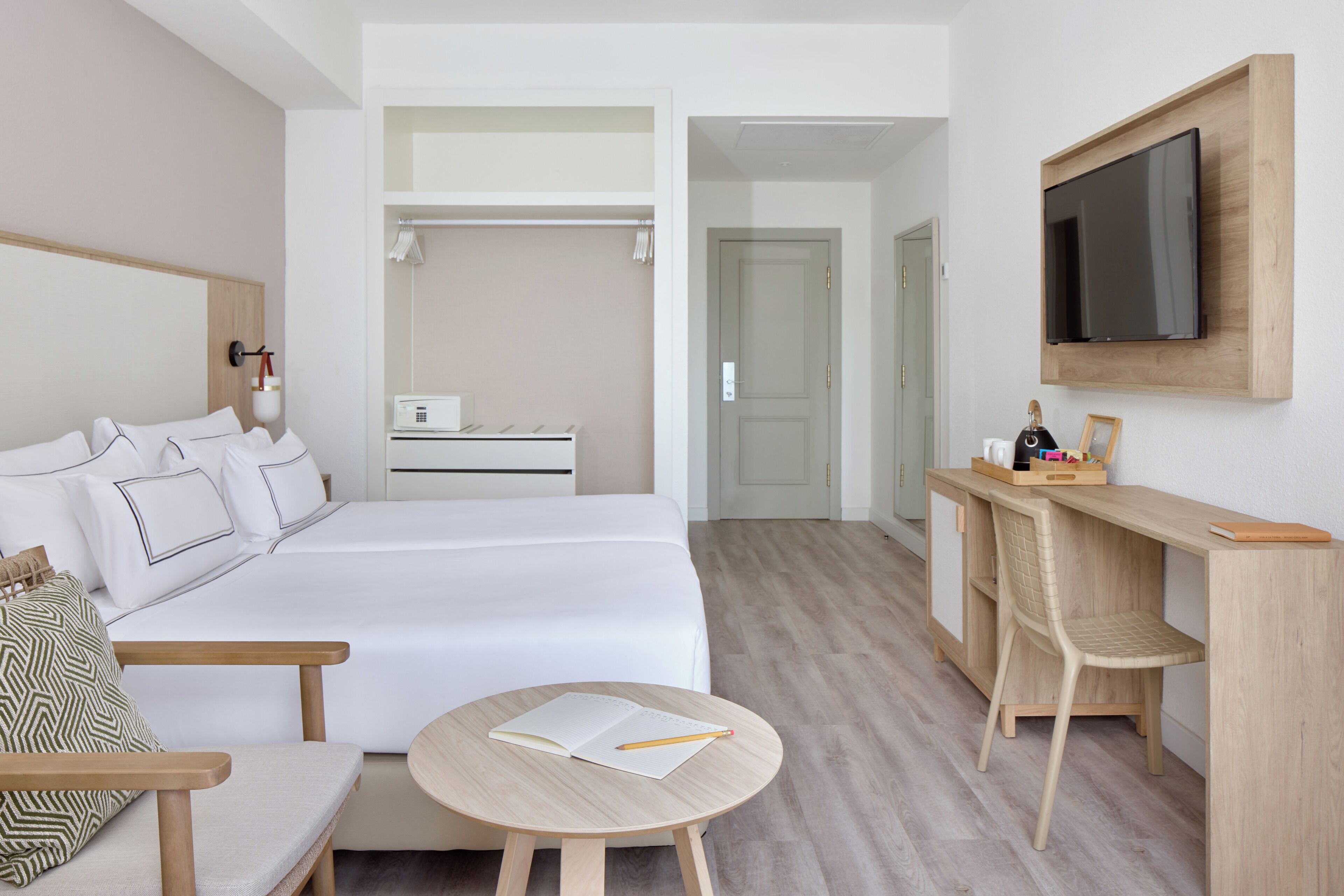 A hotel room with a bed, a desk, a chair, a round table, and a TV mounted on the wall.