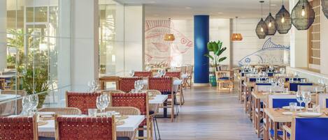 A spacious restaurant with wooden tables and chairs, large windows, and decorative wall art.