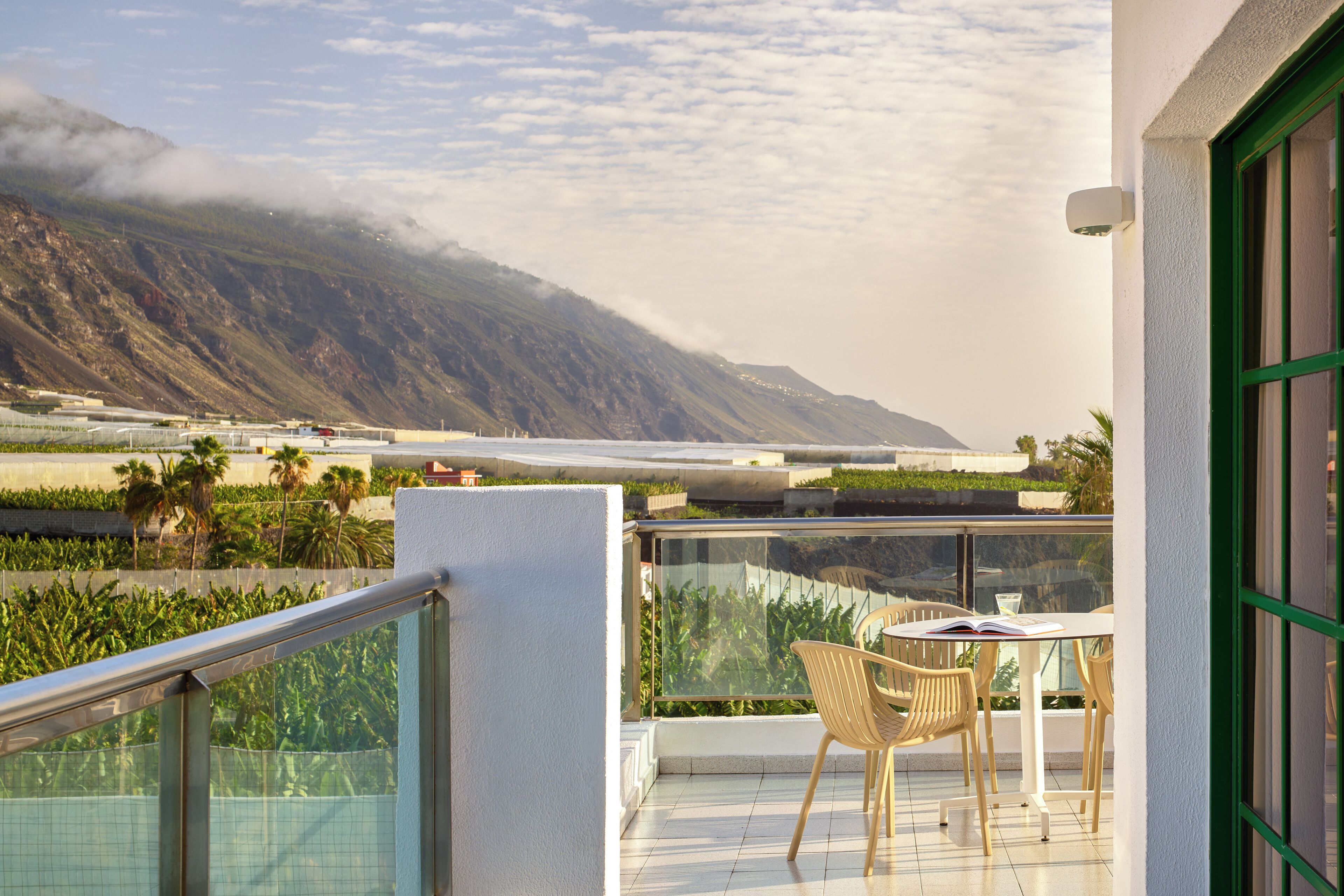 A balcony with a table and chairs, overlooking a mountainous landscape and a body of water.