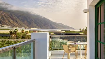 A balcony with a table and chairs, overlooking a mountainous landscape and a body of water.
