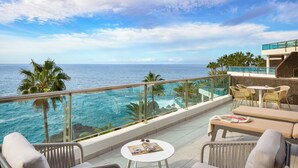 Een balkon met rieten meubilair, een kleine tafel en uitzicht op de oceaan.