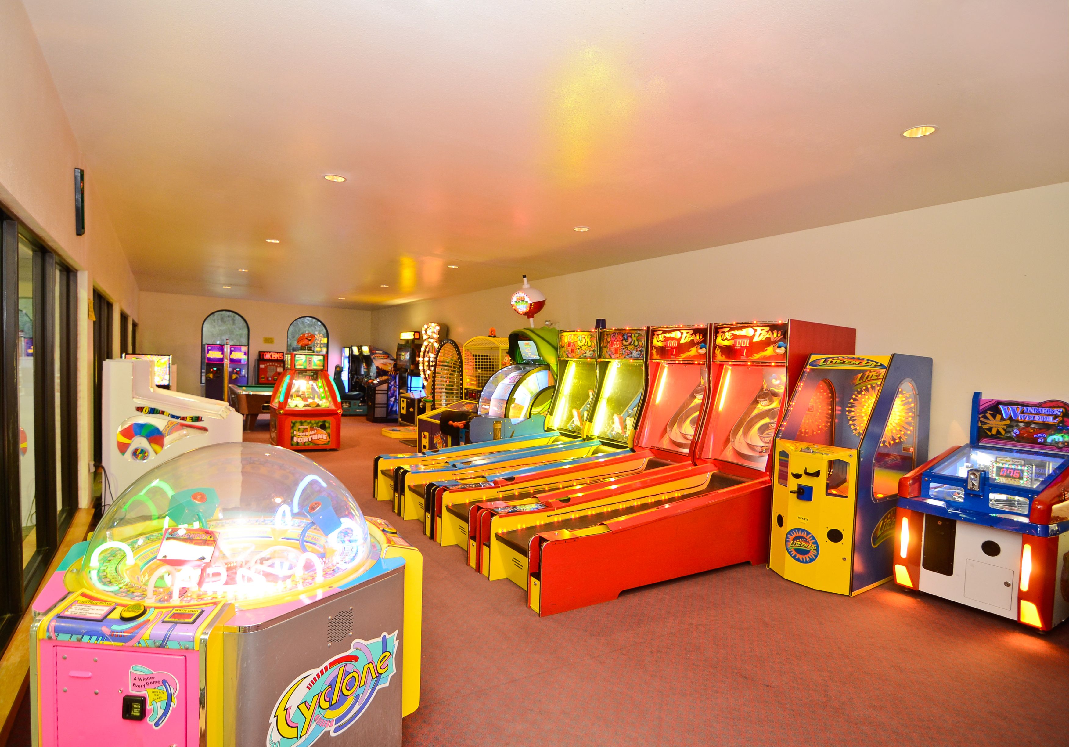 Une rangée de bornes d’arcade illuminées de couleurs vives se trouve dans une pièce dont le sol est recouvert d’une moquette et qui est séparée du reste par une cloison en verre.