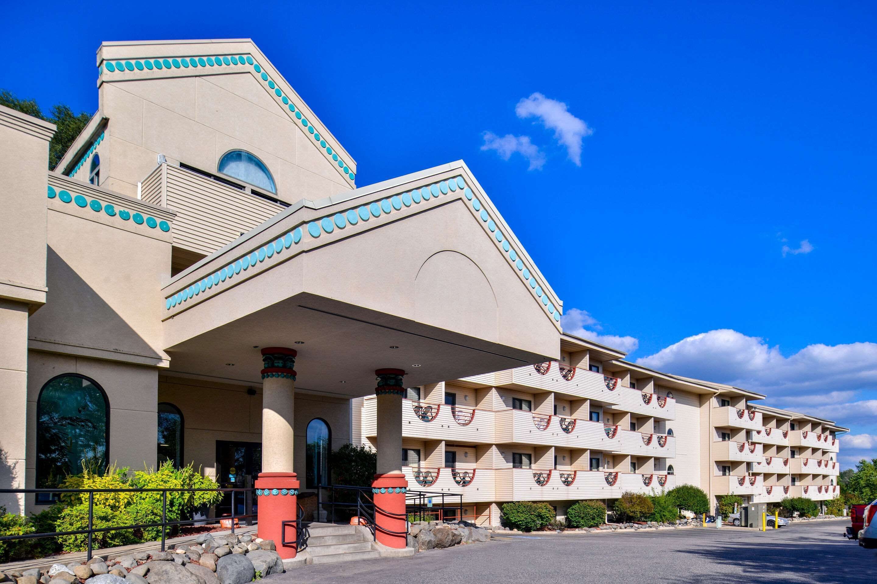 A multi-story hotel with a distinctive architectural design, featuring a central atrium, balconies with decorative railings, and a parking area in front.
