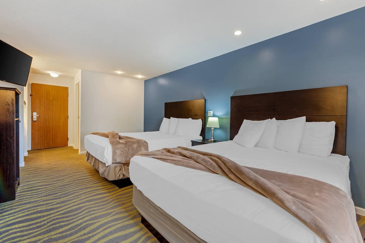 A hotel room with two beds, a wooden door, a lamp, and a carpeted floor.