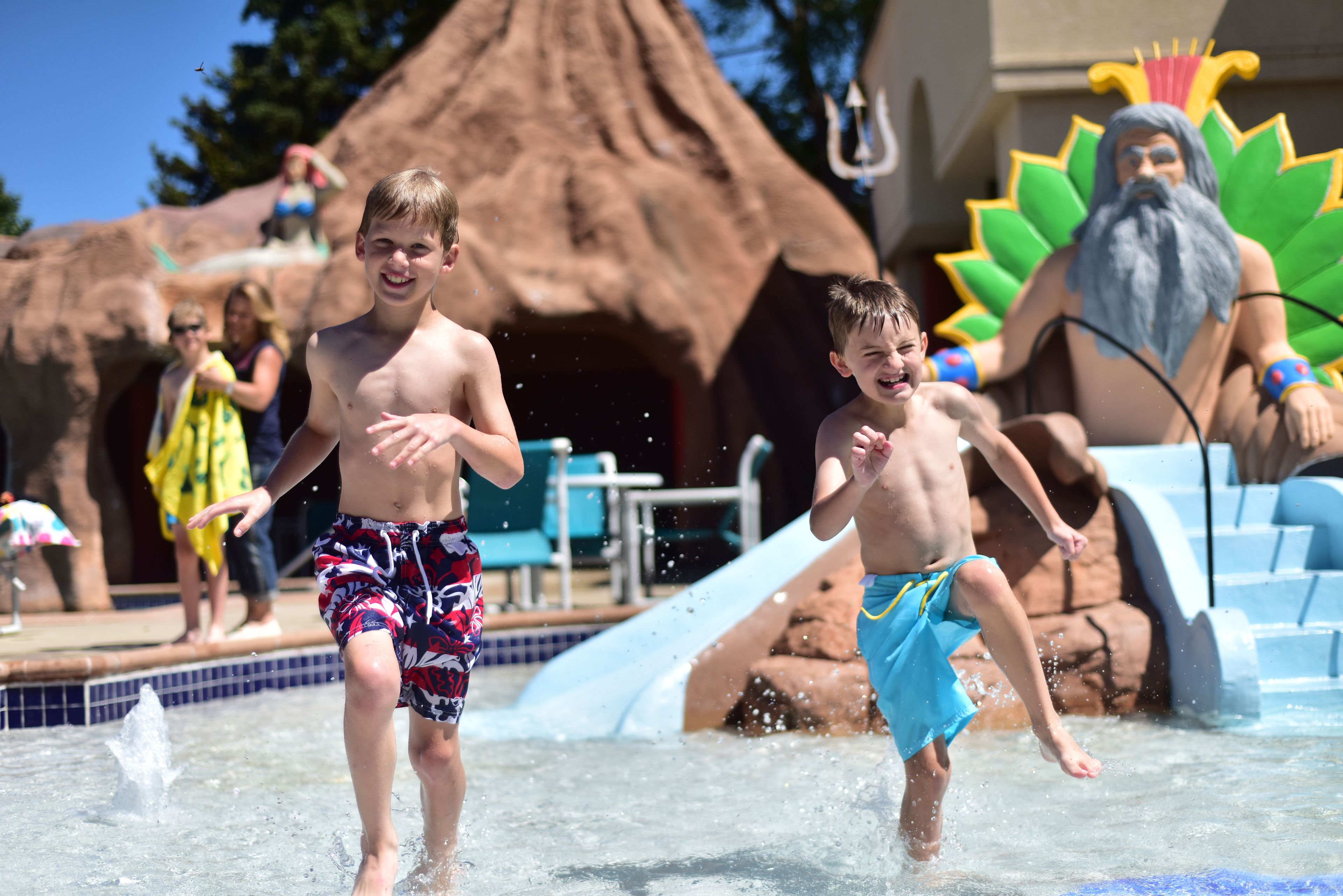 Bambini che giocano in un parco acquatico con uno scivolo e una grande statua sullo sfondo.