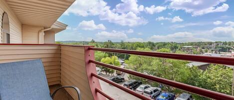 A balcony with a red railing, a blue chair, and a view of parked cars and greenery.