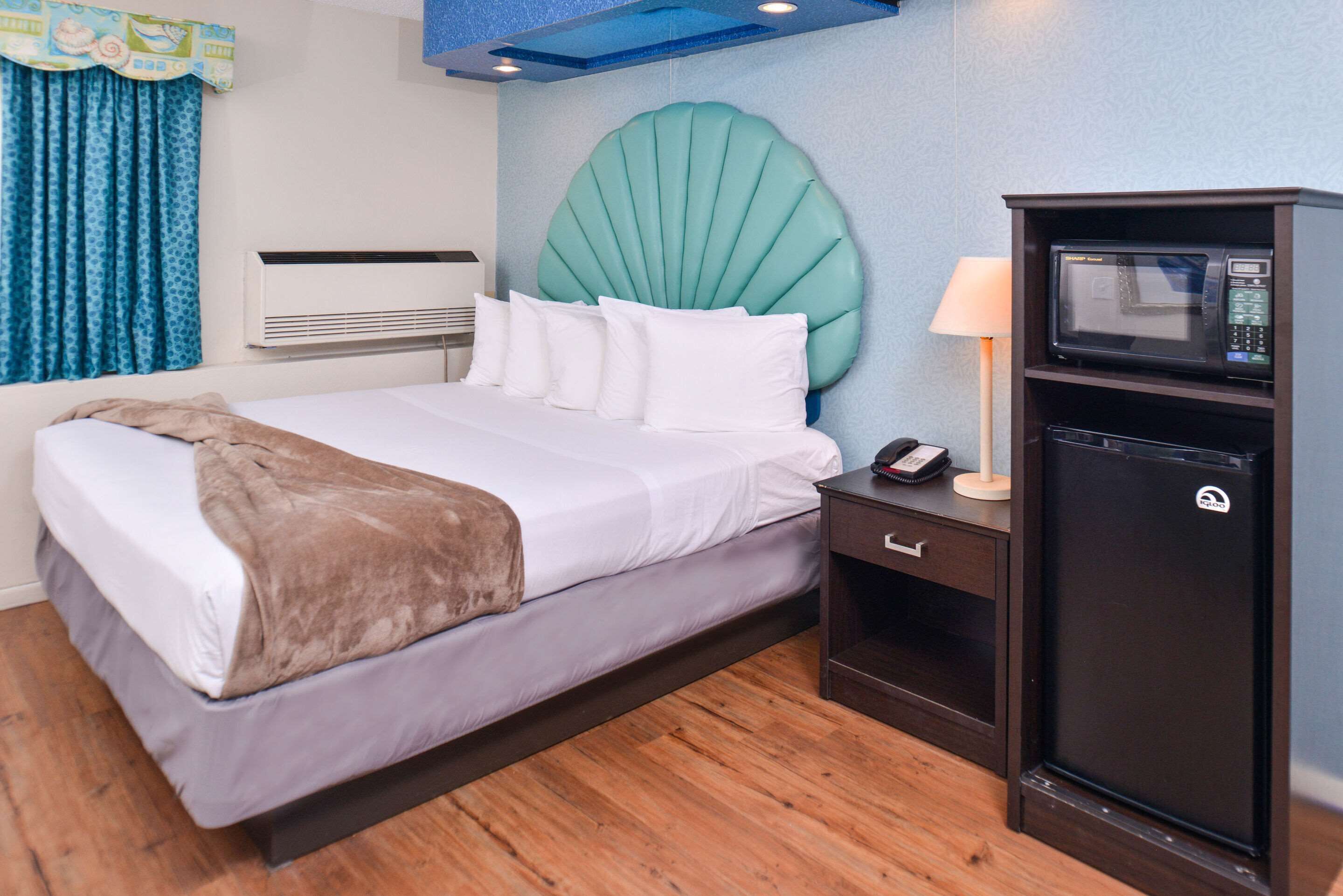 Une chambre d’hôtel équipée d’un lit, d’une tête de lit de couleur turquoise, d’un mini-bar et d’un climatiseur fixé au mur.