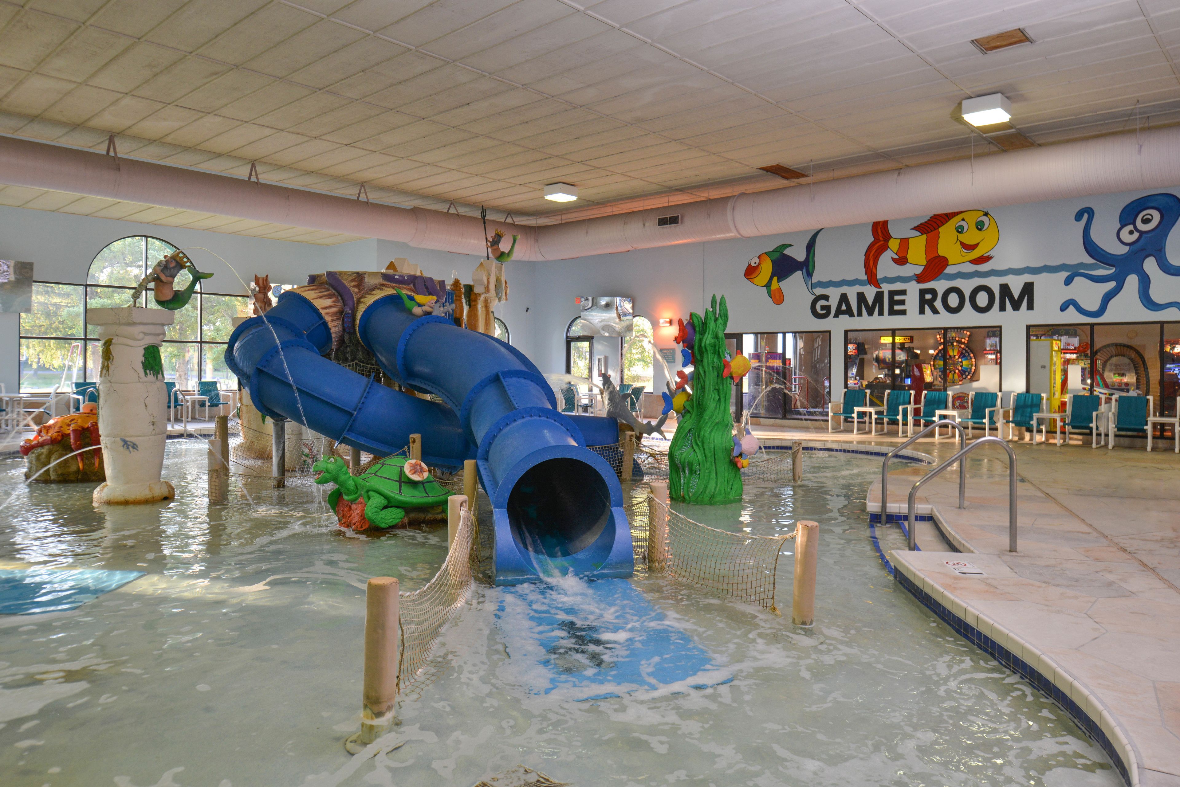 An indoor water play area with a blue slide, a pool, and a 'Game Room' sign.