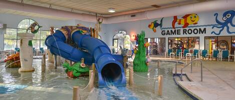 An indoor water play area with a blue slide, a pool, and a 'Game Room' sign.
