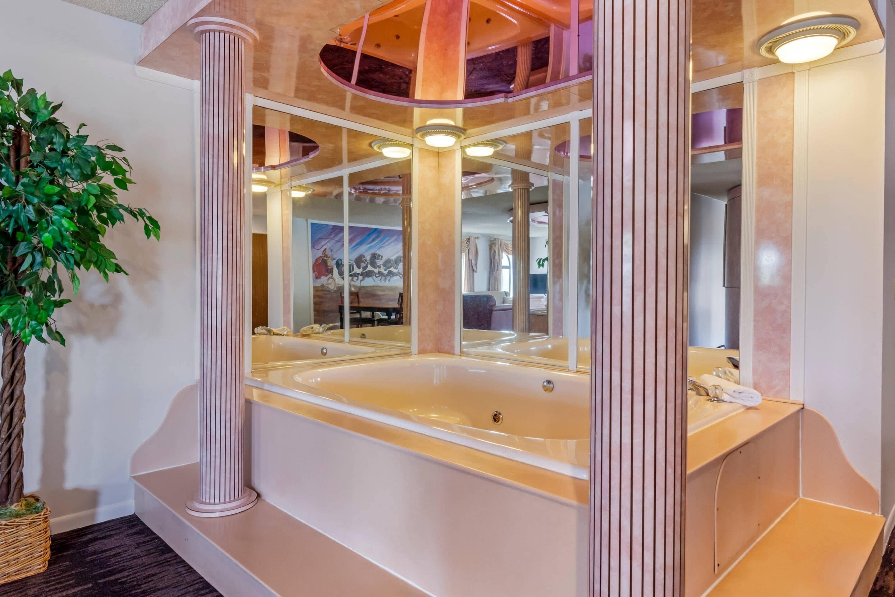 A modern bathroom with a large bathtub, a mirror, and a plant.