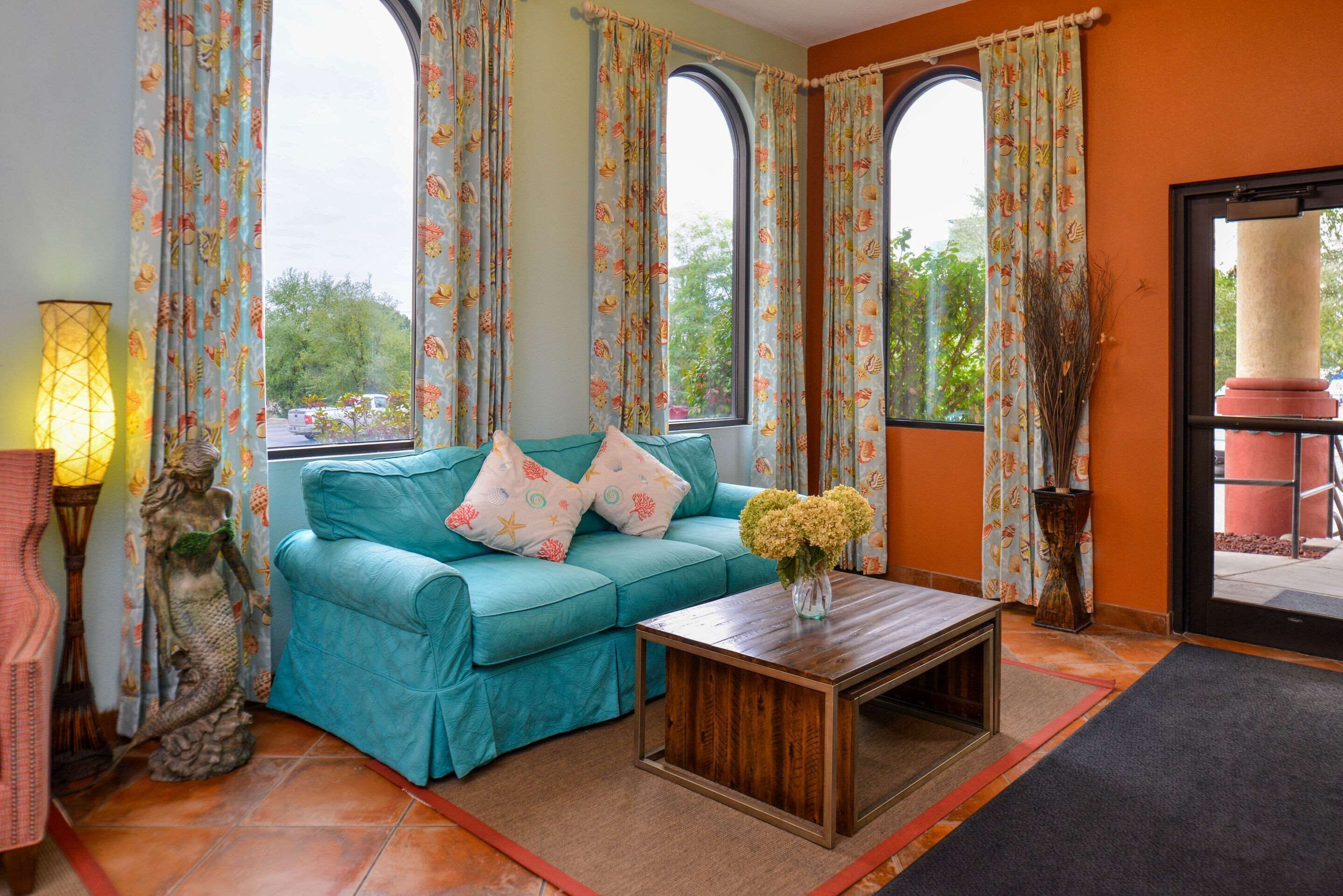 A teal sofa with patterned cushions, a wooden coffee table, and a vase of flowers.