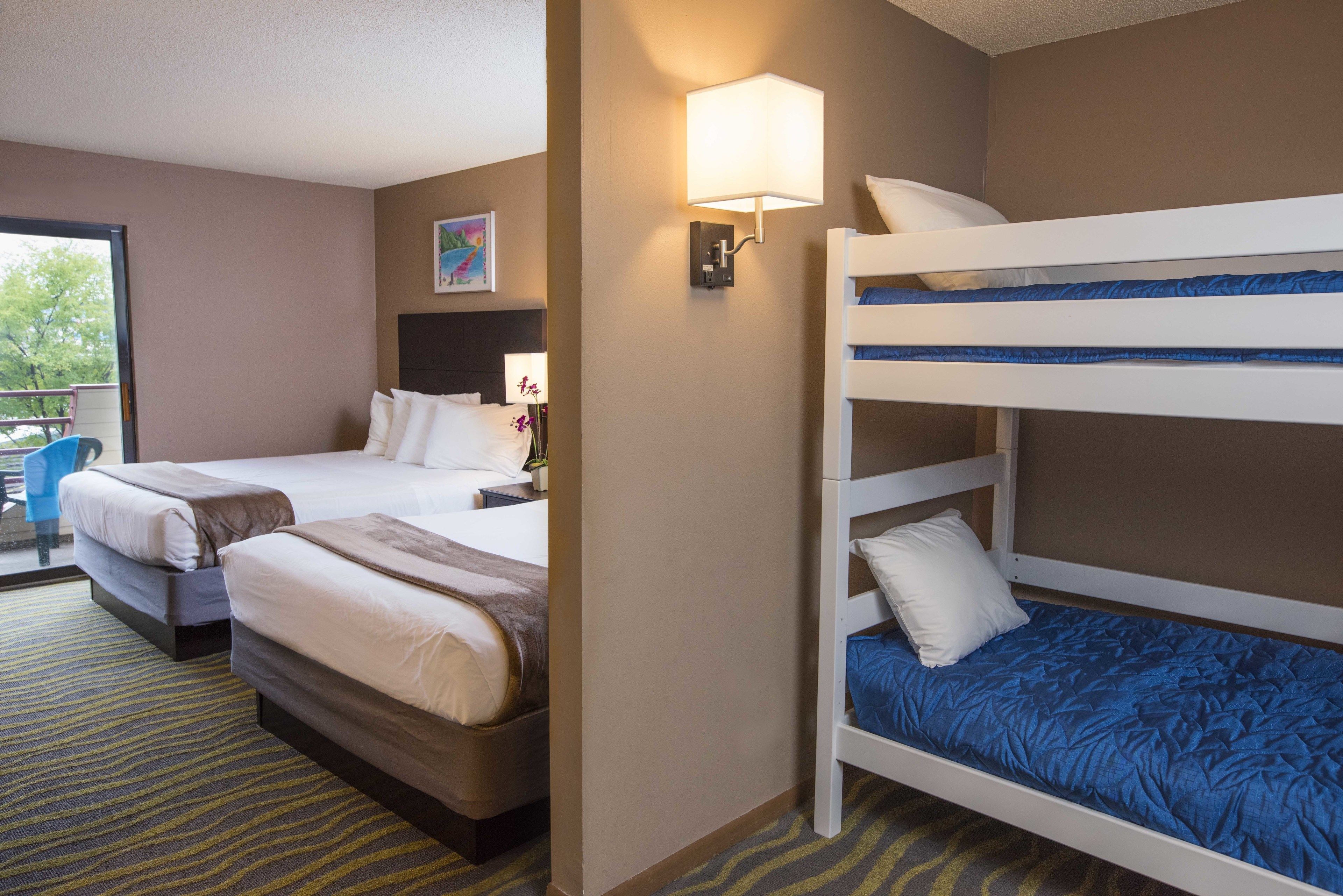 A hotel room with two beds, a window, and a wall-mounted lamp.