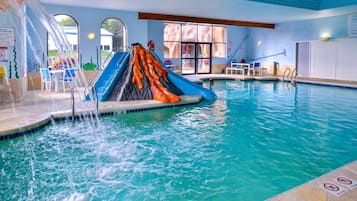 Enjoy a refreshing swim in our indoor pool with a central slide, lifeguard stand, and seating area with tables and chairs.