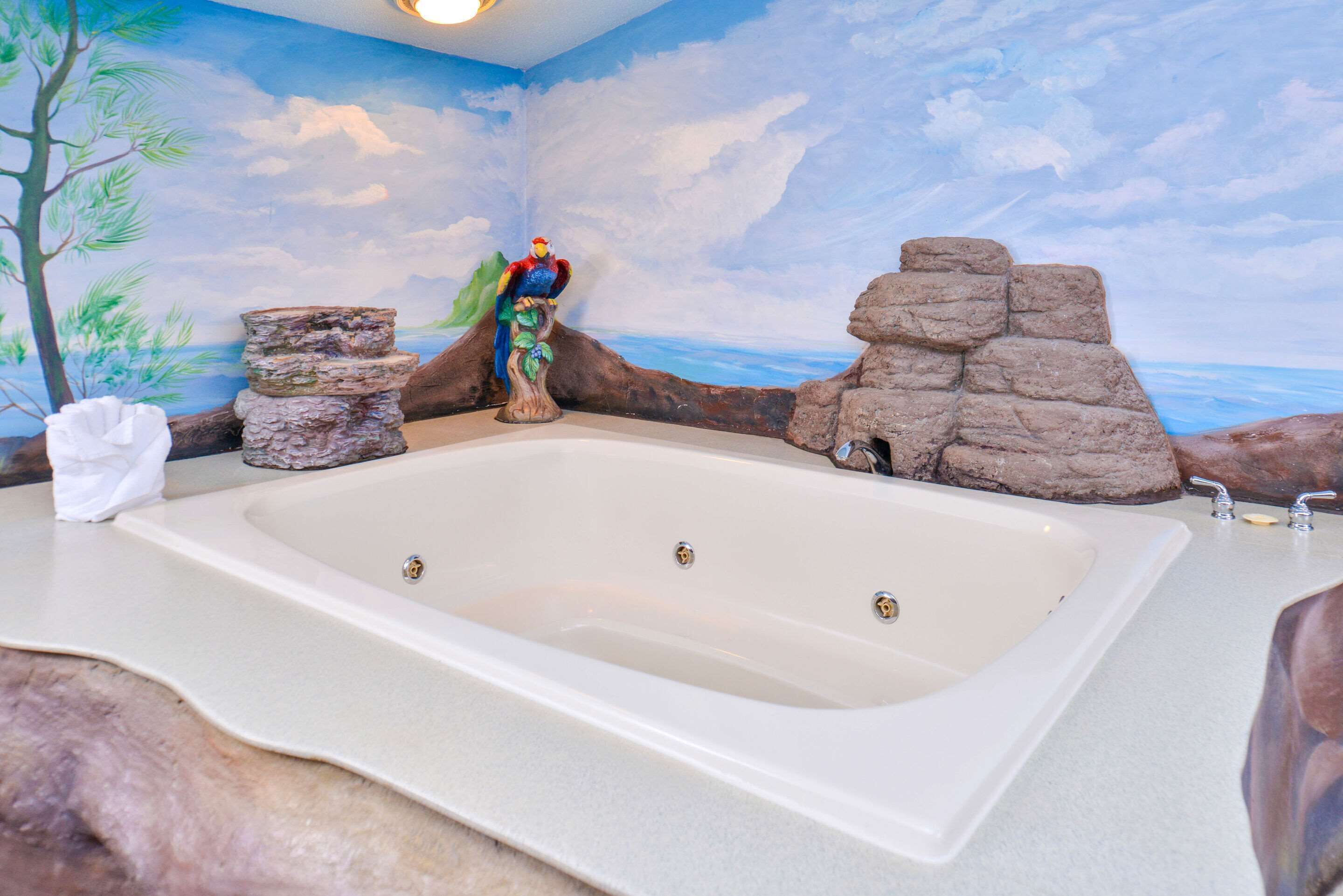 Une salle de bain avec une grande baignoire, un arbre décoratif et une fresque murale représentant une scène de plage.