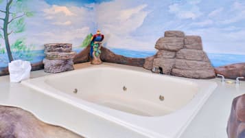 Une salle de bain avec une grande baignoire, un arbre décoratif et une fresque murale représentant une scène de plage.
